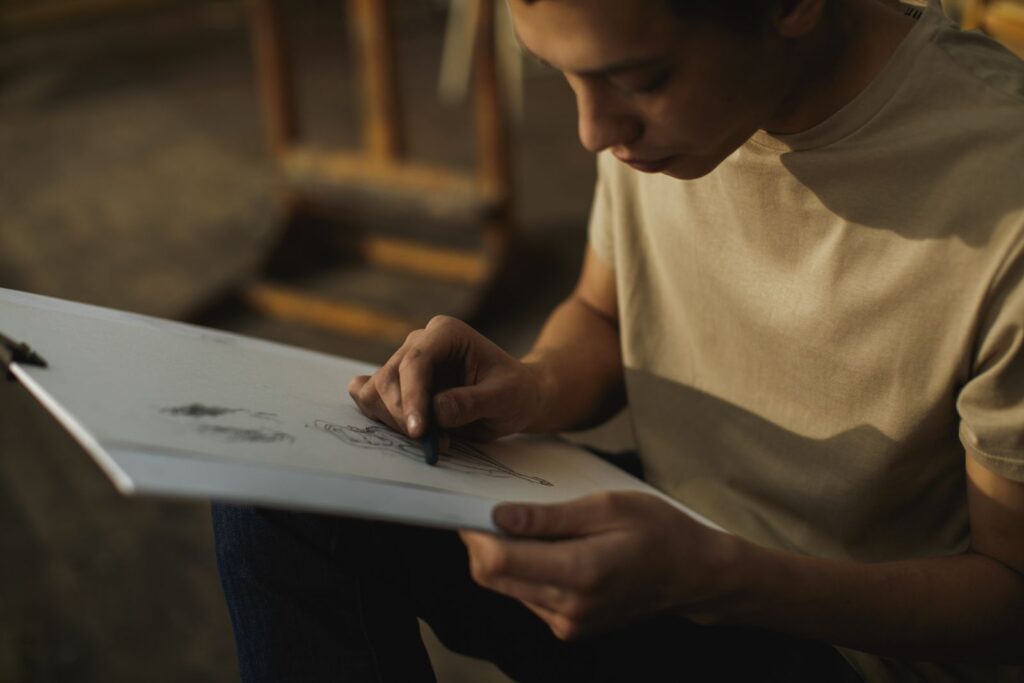 Adulte concentré s'exerçant au dessin au fusain sur un carnet de croquis dans un atelier