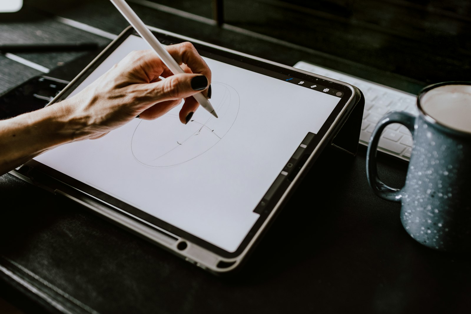 Main dessinant avec un stylet sur une tablette graphique posée près d'une tasse